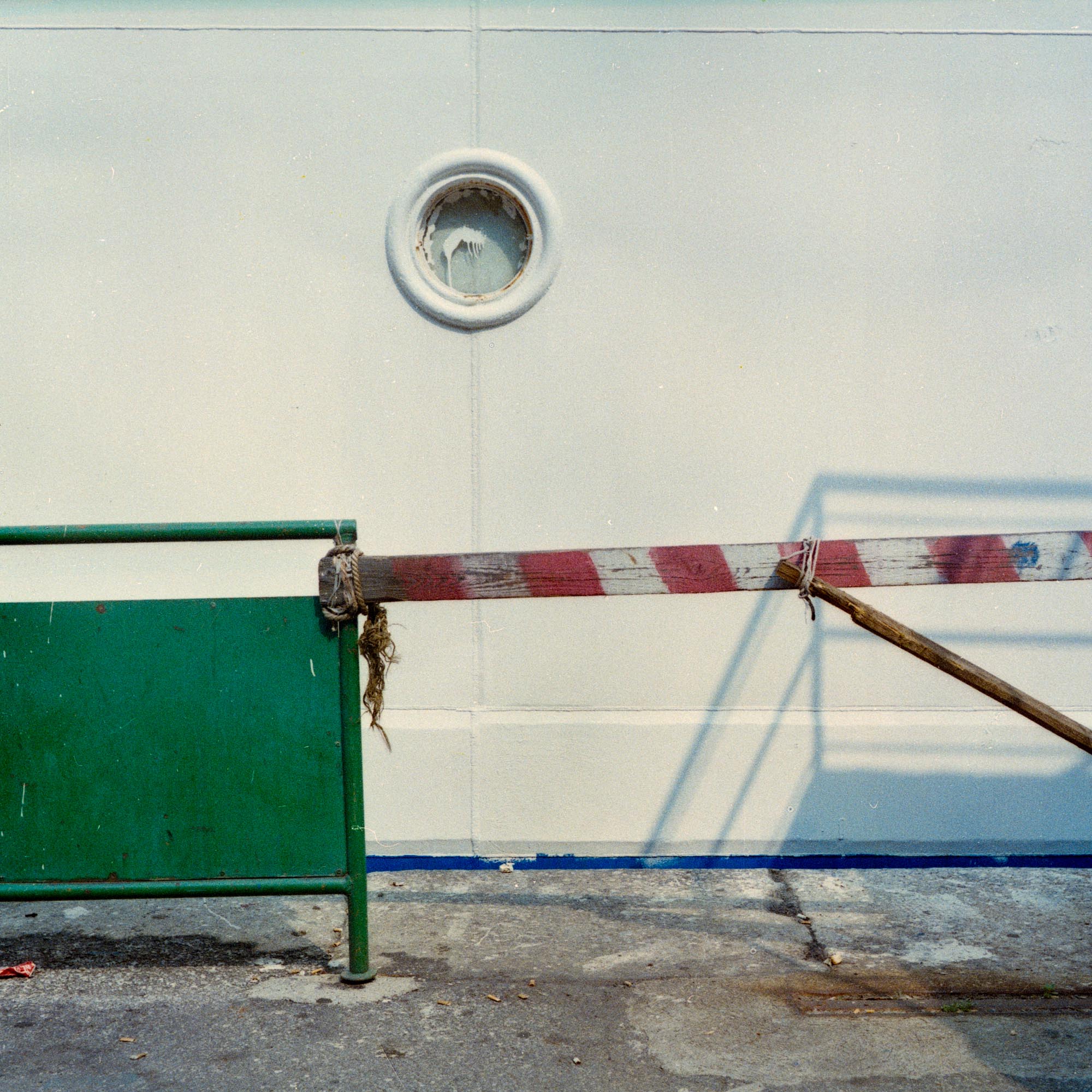 red white strip green toll caution circle shadow blue wall stick panel rope string concrete pavement window rust formalism
